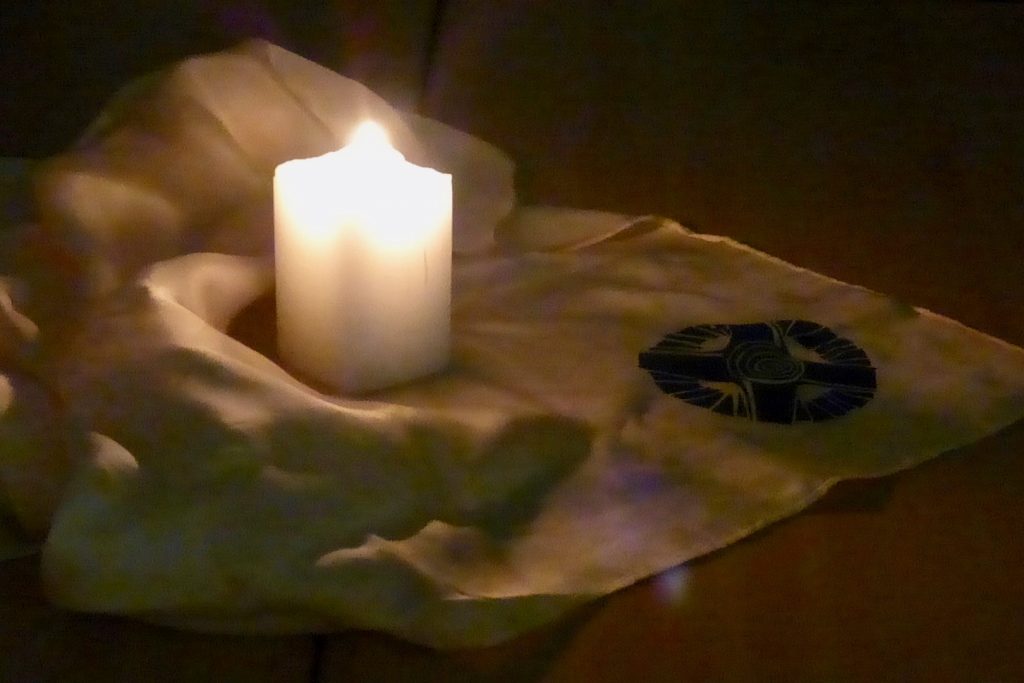Eine brennende Kerze auf Tuch mit eingesticktem Kreuz